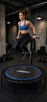 Woman exercising on a Bungee Fit trampoline with blue trim in an indoor gym.