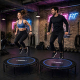 Two adults exercising on separate Bungee Fit fitness trampolines in a studio.
